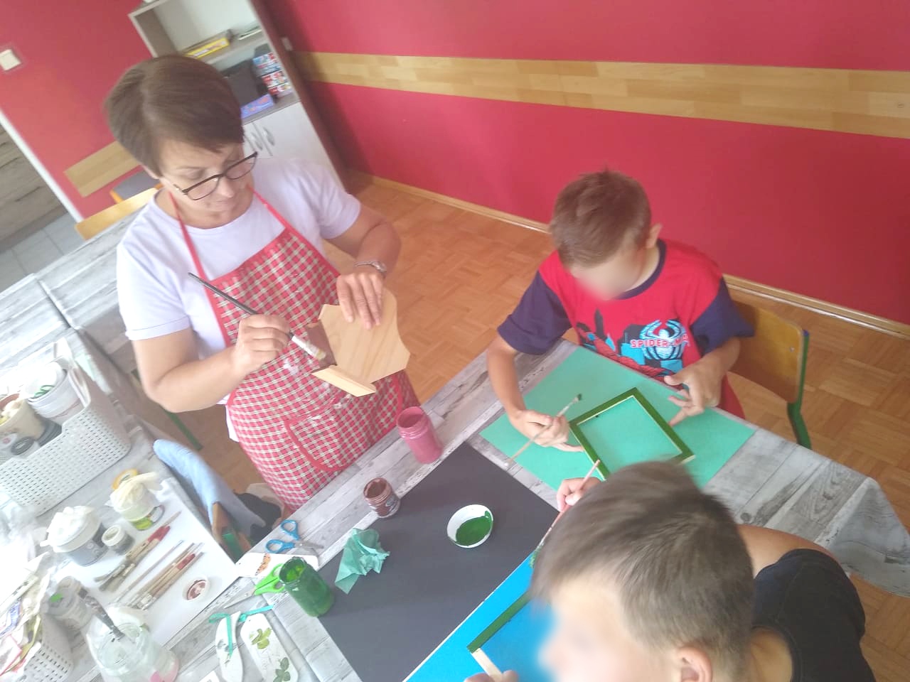 Pani Magda pokazuje dzieciom jak malować drewno