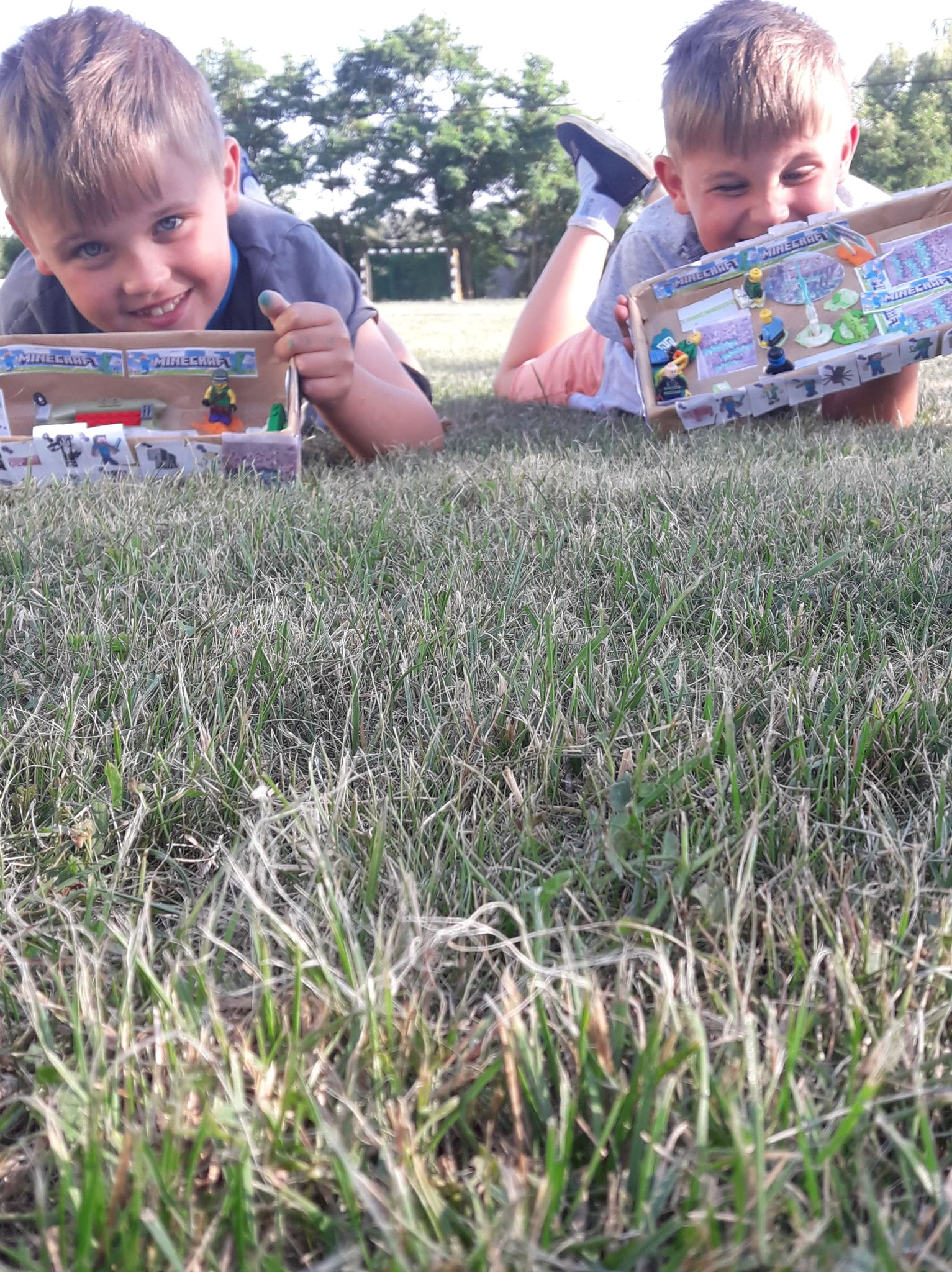 chłopcy leżą na trawie i chwalą się pudełkami