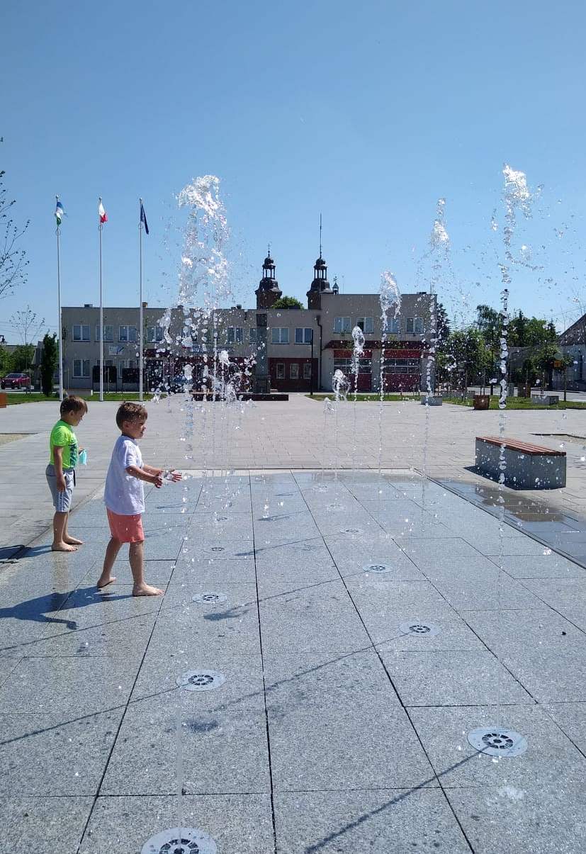 chłopcy bawiący się na fontannach na rynku w tle urząd gminy i kościół