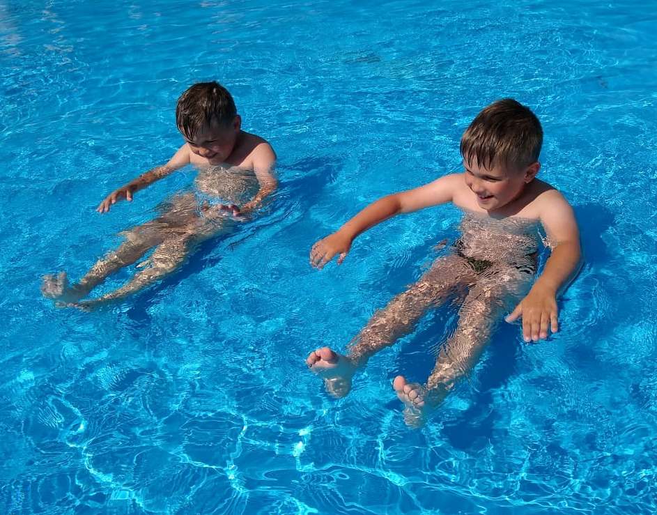 chłopcy siedzą w basenie, unoszą ręcę i nogi